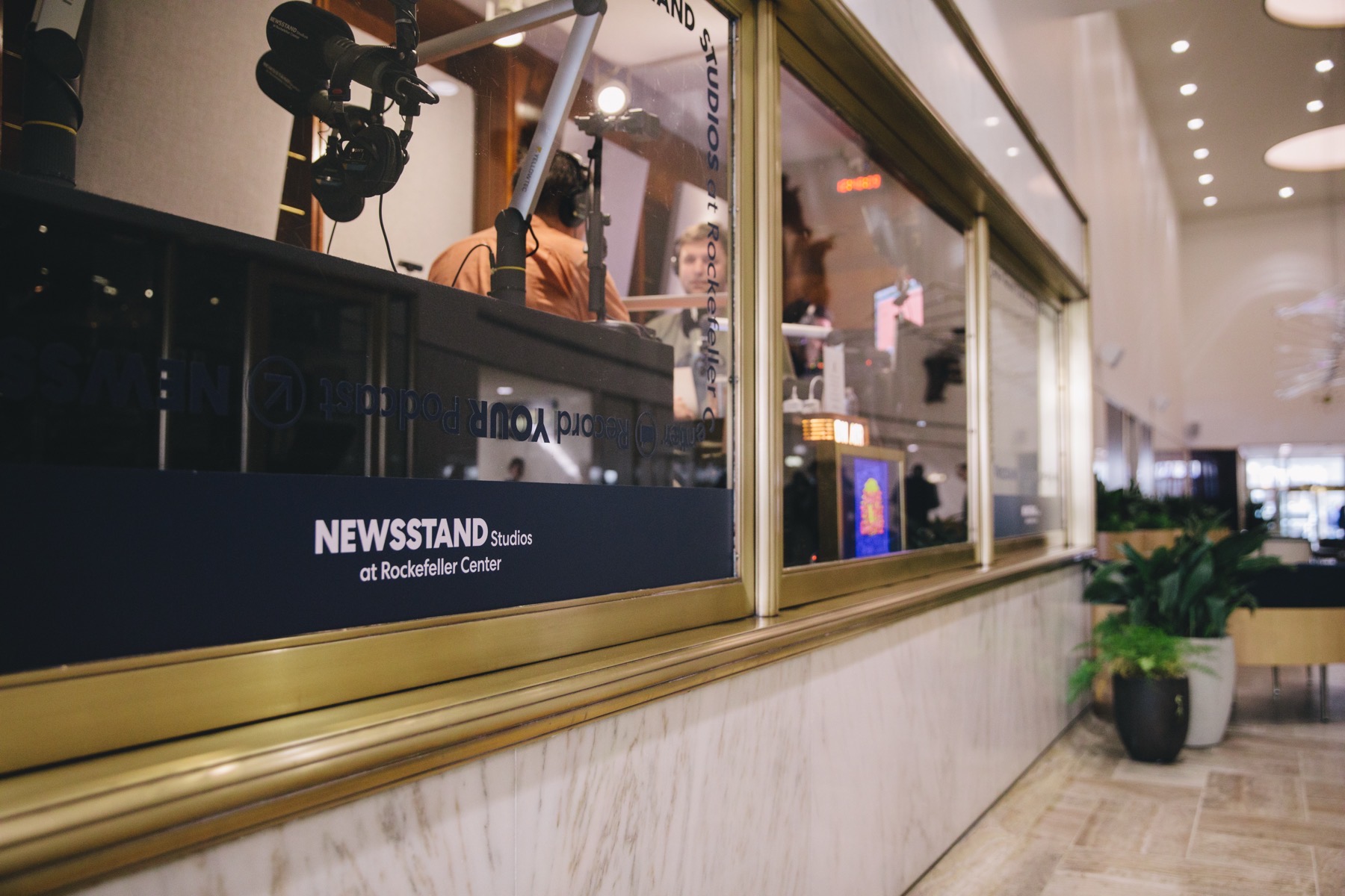 The brass and glass window of Newsstand Studios in the marble lobby of Rockefeller Center, microphones visible inside